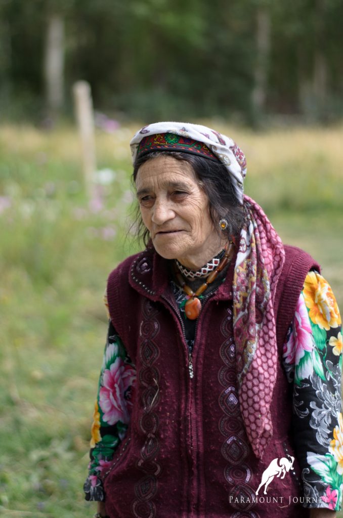 An elderly Pamiri woman in traditional attire, standing outdoors in Gorno-Badakhshan, Tajikistan, reflecting the unique cultural identity of the Pamir region