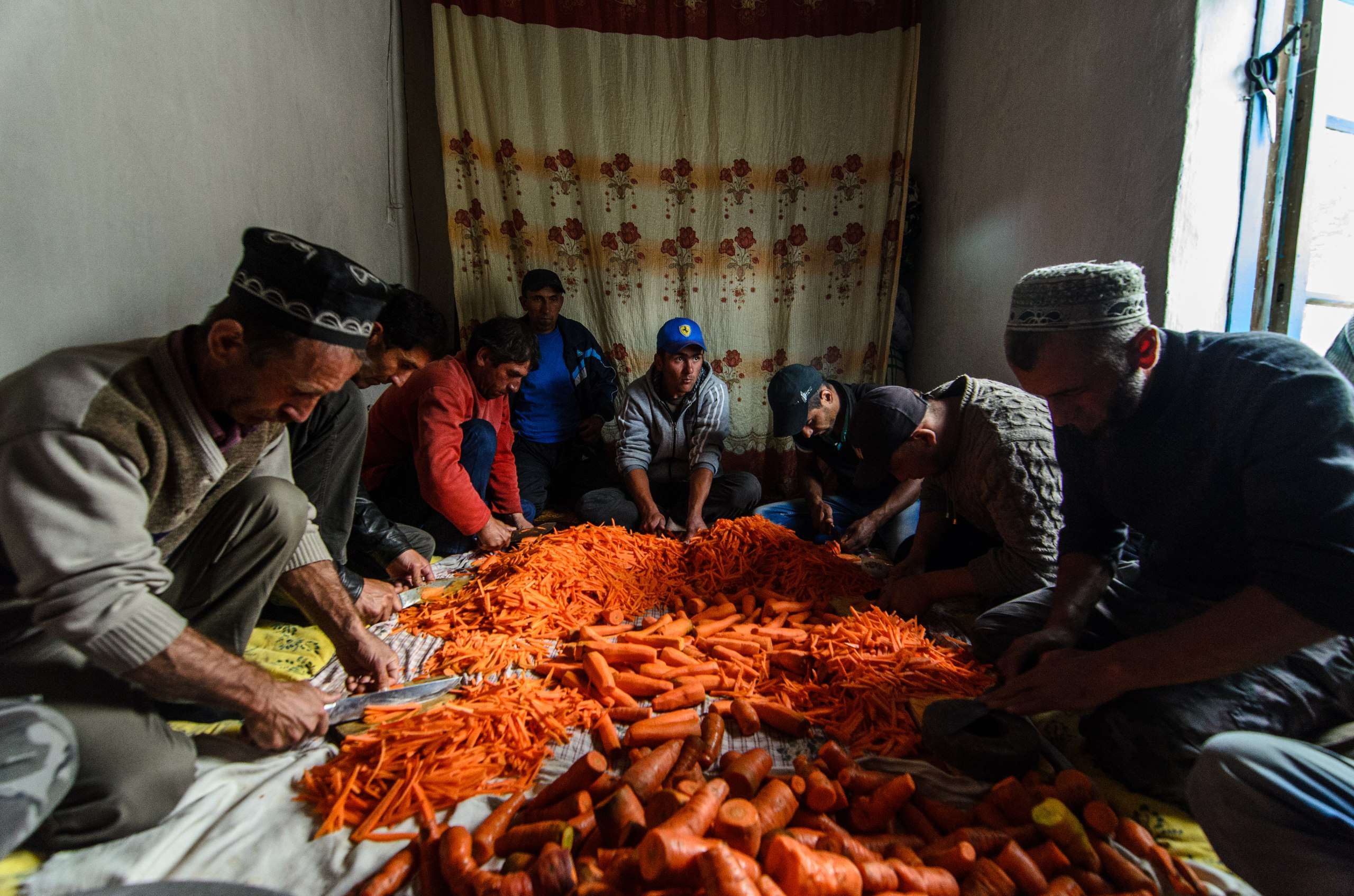 Tajik men gathered in a traditional setting to cut carrots for plov, a ceremonial dish, as part of wedding preparations.