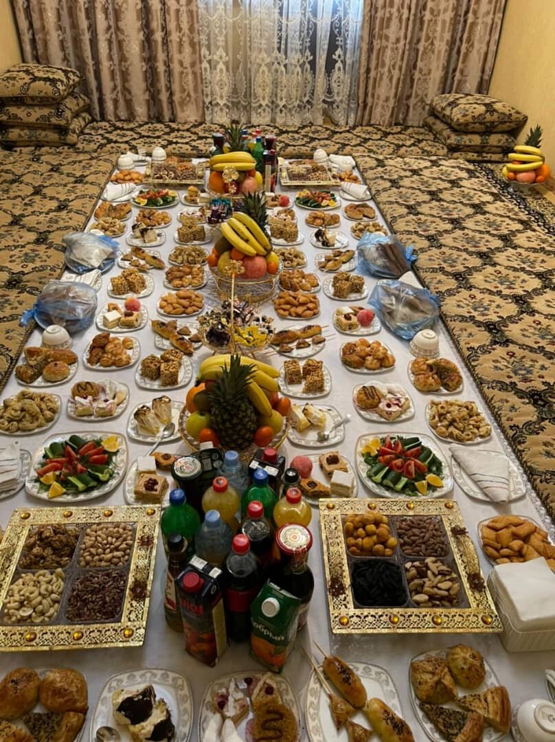 Luxurious Tajik dastarkhon spread with traditional sweets, dried fruits, nuts, pastries, fresh fruits and beverages arranged on an ornate tablecloth with decorative serving trays