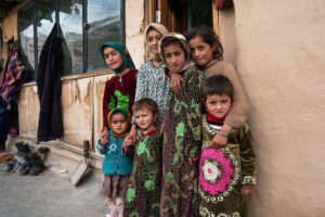 Yagnobi children in colorful traditional dress stand together outside a village home