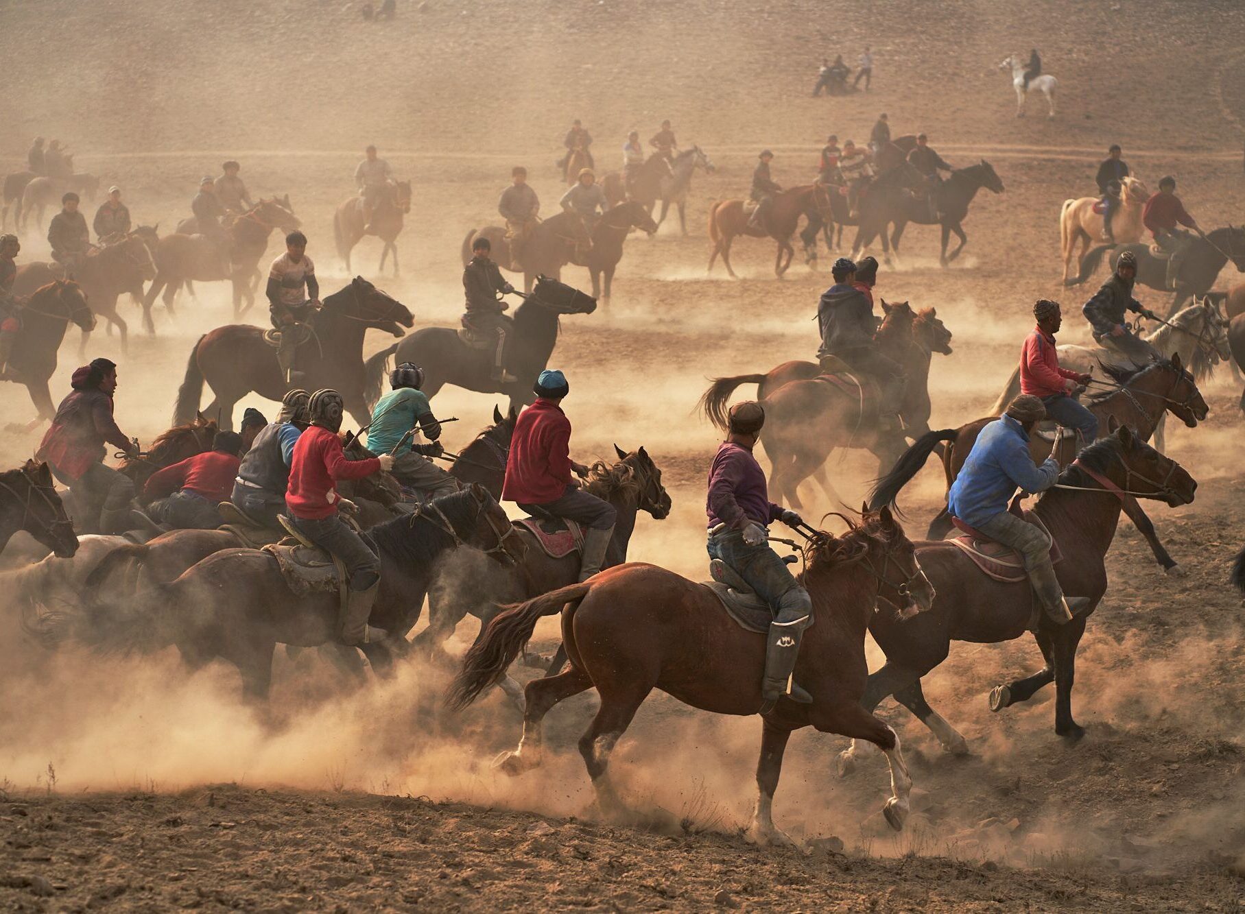Intense buzkashi scrum with dozens of riders in colorful traditional clothing competing on horseback amid massive dust clouds during traditional equestrian tournament